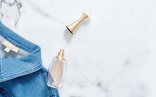 Jean jacket with open perfume bottle on it's side sitting next to it