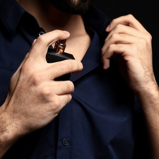 man in black buttoned up dress shirt spraying cologne on his collar bone