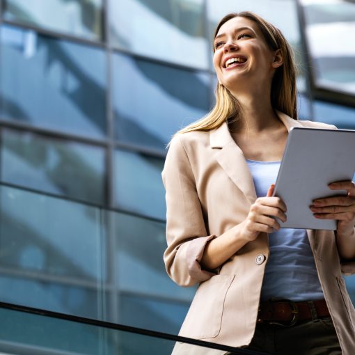 smiling blonde woman in a taupe colored blazer holding an ipad