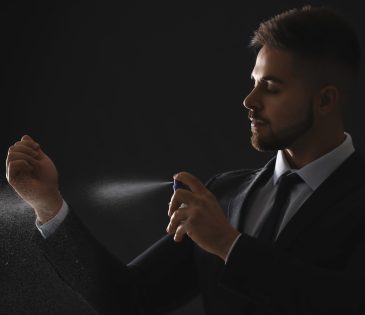 Silhouette of handsome young man with bottle of perfume on dark background