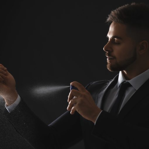 Silhouette of handsome young man with bottle of perfume on dark background