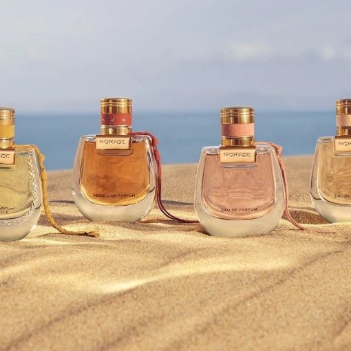 a line of 4 Chloe Nomade perfume bottles on a beach