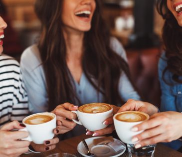 Three young women smiling and enjoying coffee at a coffee shop