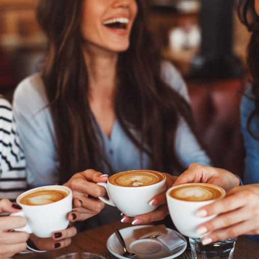 Three young women smiling and enjoying coffee at a coffee shop