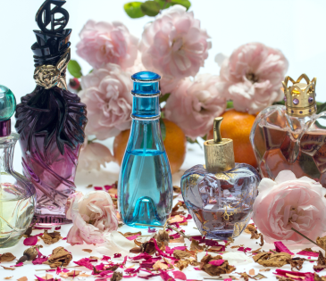 an abundance of perfume bottles sitting on dried up rose petals with pink flowers in the background