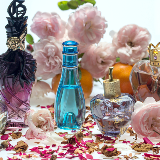 an abundance of perfume bottles sitting on dried up rose petals with pink flowers in the background
