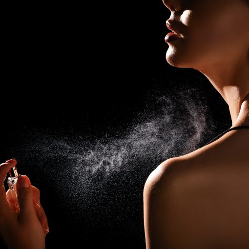 Woman spraying luxury perfume on black background, closeup