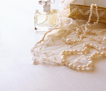 vintage perfume bottle next to a string of pearls, lace fabric, and an antique box