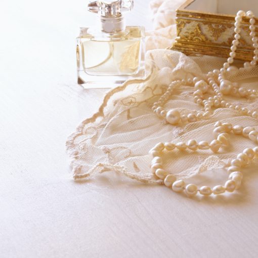 vintage perfume bottle next to a string of pearls, lace fabric, and an antique box