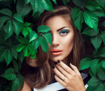 beautiful brunette standing in a bunch of green leaves featuring a Green Eye Makeup Look