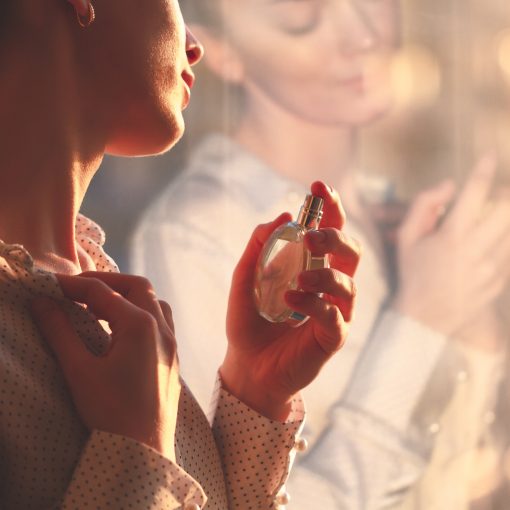 Stylish woman in blouse spraying a bottle of favorite perfume at sunset