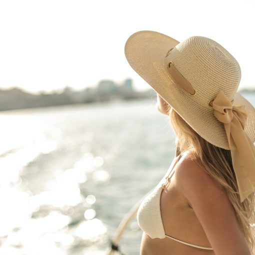 A woman stands in a yacht, wearing a white sun hat and an off-white bra top.