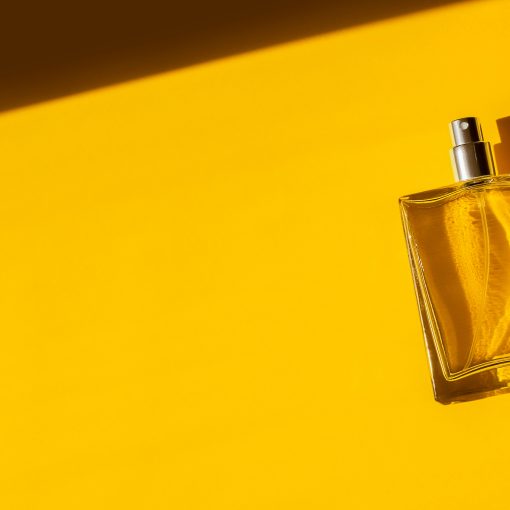 Transparent bottle of perfume on a yellow background. Fragrance presentation with daylight. Trending concept in natural materials with beautiful shadow. Women's essence.