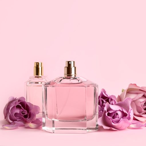 Bottles of perfume and beautiful roses on pink background